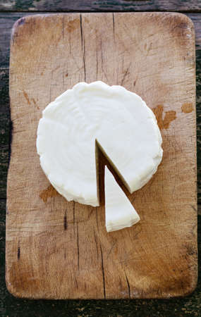 Round fresh cheese with a cut portion. Top view of a cheese on a wooden board.の写真素材