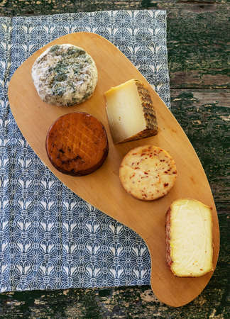 Top view of assorted cheeses on a rustic wooden board. Blue cheese, cured cheese, Manchego cheese, smoked cheese.の写真素材