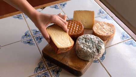 ga cheese from a table with a variety of cheeses, on a rustic tile countertop.の写真素材