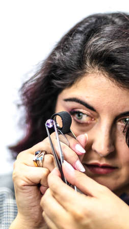 Gemologist woman observes a precious stone with her magnifying glass while holding it with her...