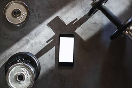 Mobile phone with white screen on a surface with dumbbells and different iron weight plates