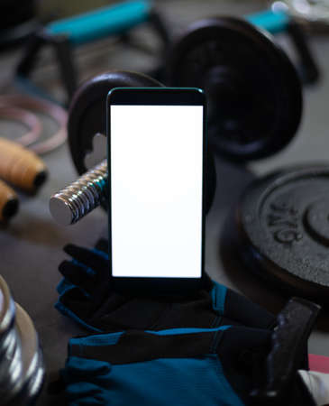 Mobile phone surrounded by different elements for sports training such as dumbbells, plates for...