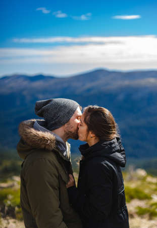 Young couple in love and in winter clothes kiss in front of the mountain rangeの写真素材