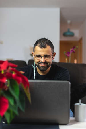 Man works from home with his laptop using earphones with a pretty red poinsettia flower in frontの写真素材