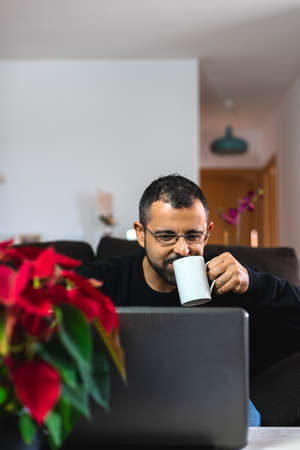 Happy man with his laptop from home with a nice red poinsettia drink from a cupの写真素材