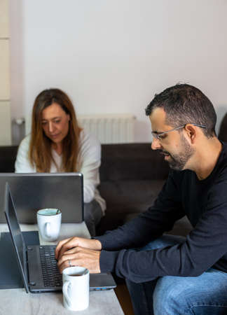 Young couple working from home sitting on the couch with their laptopsの写真素材