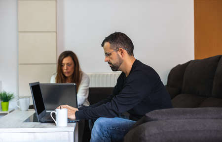 Young couple working from home sitting on the couch with their laptopsの写真素材