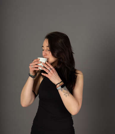 Alternative young woman with tattoos and smartwatch drinks coffee from a recyclable cupの写真素材