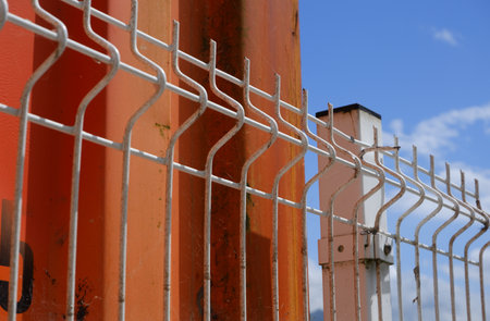 Industrial red container and white fence with blue sky behindの写真素材