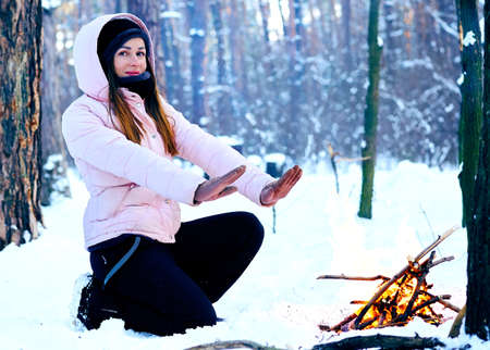 Young woman on a winter picnic in the forest warming up near the fire