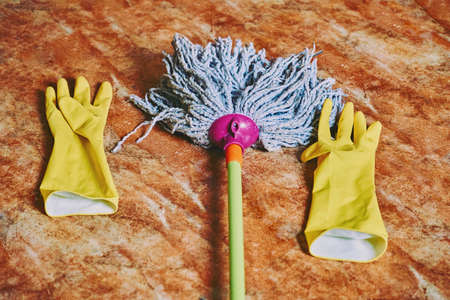 Two yellow household gloves and mop on a clean marble floorの写真素材