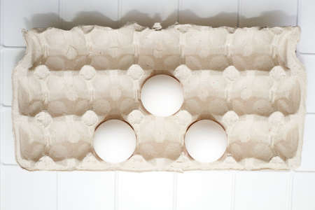 Three white eggs in a cardboard tray on a white background