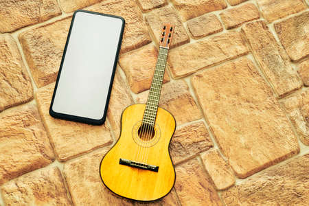 Phone with space for text, acoustic guitar on a cobbled yellow sand backgroundの写真素材