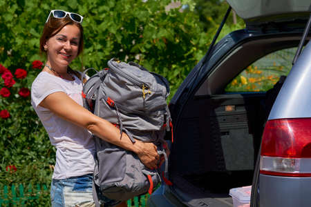 A young woman puts a backpack and other things in the car going on a tour.の写真素材