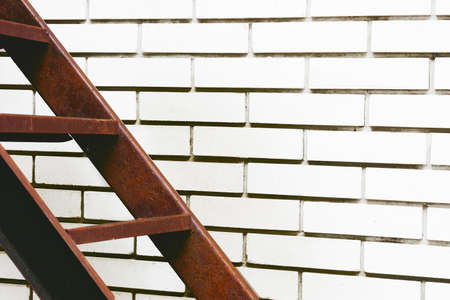 Part of the stairs red metal ladder leading up against of a white brick wallの写真素材