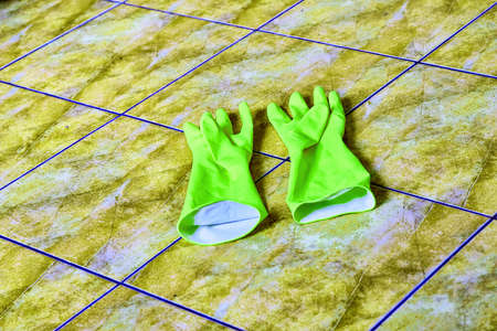 Two bright green household gloves on a dirty yellow poisonous floorの写真素材
