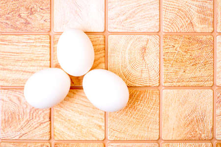 Three chicken bird eggs on a wooden pink orange checkered surfaceの写真素材