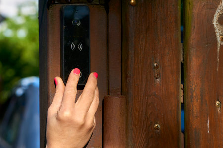 Womans hand pressing a doorbell on a wooden fence in the garden