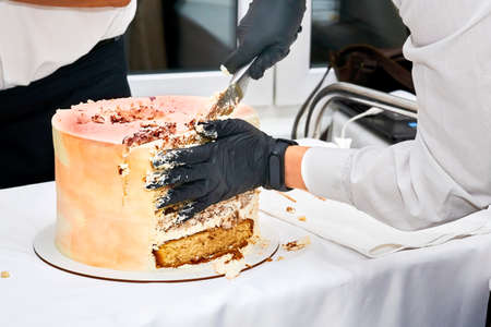 Cutting a delicious birthday cake on a serving table in protective gloves