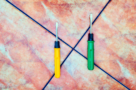 Green and orange screwdrivers on red marble tiles.の写真素材