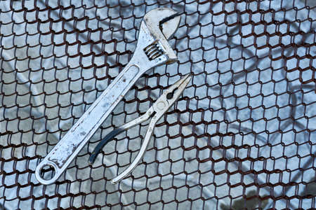 Adjustable wrench and pliers on a metal rusty grid
