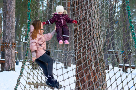 Cheerful mother with a child on a playing net stretched on trees in a winter parkの写真素材