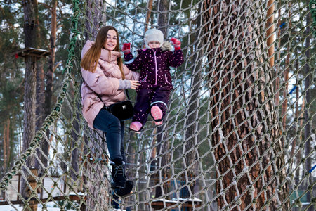 Cheerful mother with a child on a playing net stretched on trees in winter parkの写真素材
