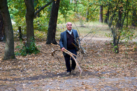 An elderly cheerful man cleans the forest park from branches. Collects firewoodの写真素材
