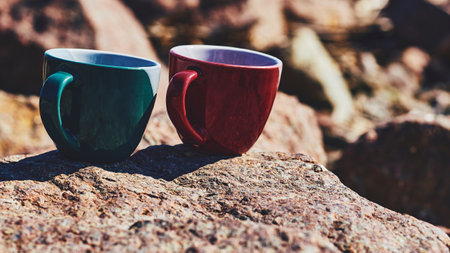 Red green ceramic cups for coffee tea beverages on a rocky sunny stonesの写真素材