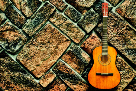 Yellow orange acoustic guitar on gray brown dark brick wallの写真素材