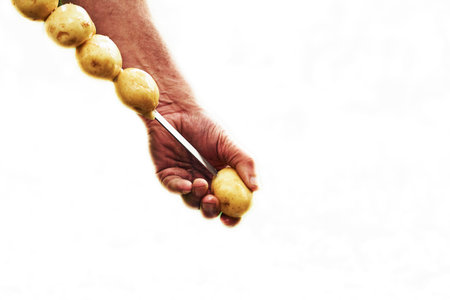 Hands of a man stringing potatoes on a skewer for grilling on whiteの写真素材
