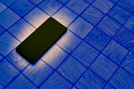Glowing black mobile phone on a checkered tiled dark blue surfaceの写真素材