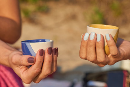 Two female hands with manicured nails holding cups with a drinkの写真素材