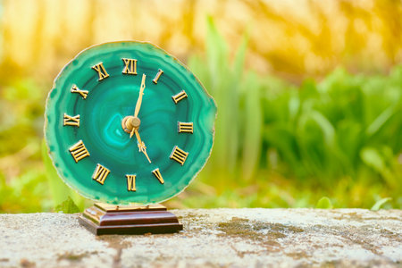 Clock with emerald dial. Gold numbers and arrows. Old stone among greeneryの写真素材
