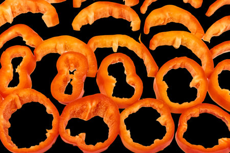 Red sweet ripe pepper cut into circles,slices on blackの写真素材