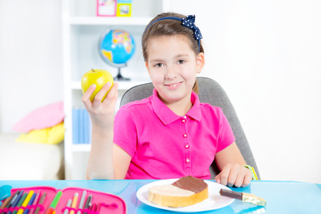 Happy smiling little girl looking a slice of bread with chocolate spread for snackの写真素材