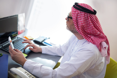 Arabian business man in his home office using smart phone and computerの写真素材