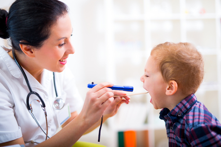 Medical doctor with child in office. Pediatrician examining little boy's throat with tongue depressorの写真素材
