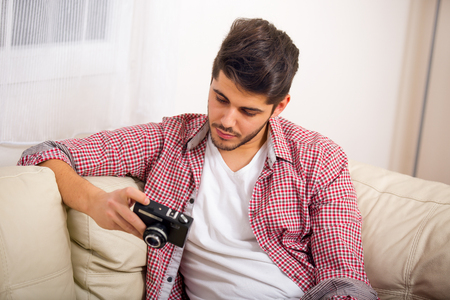 Man holding retro camera, sitting on sofa at homeの写真素材