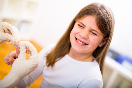 Doctor in her practice putting a bandage on some hurt of a little girl child, close upの写真素材