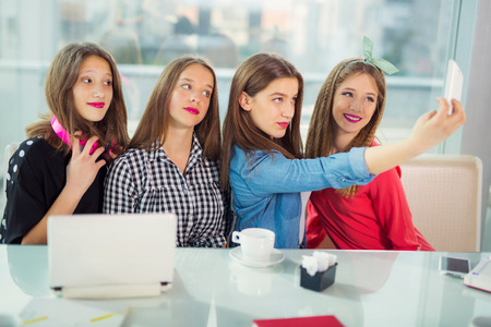 Portrait of four young women sitting at the table in the cafe take selfie with smart phone, selective focusの写真素材