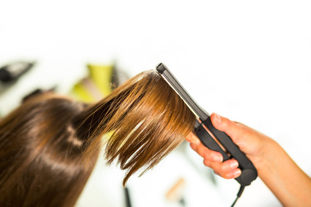 Close-up of a hairdresser straightening long blonde hair with hair irons.