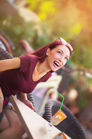Young beautiful red hair woman drinking coffee in summer cafe outdoorsの写真素材