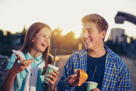 Two cheerful teenagers, girl and boy, eating pizza outdoorの写真素材