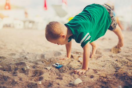 Kid playing with toy cars sitting outdoors at pebble beach against the sea beachの写真素材