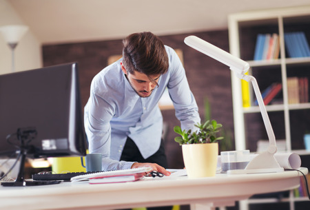 Handsome young smiling businessman working with documents in officeの写真素材