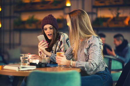 Two friends enjoying coffee together in a coffee shop and using phoneの写真素材
