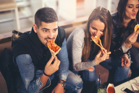 Young people in casual clothes eating pizza, talking, laughing and drinking while resting