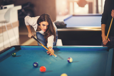 Young beautiful young woman aiming to take the snooker shot while leaning over the table in a club