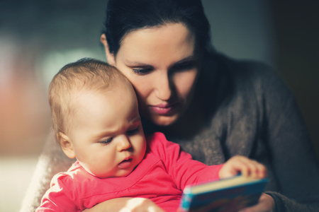 Charming mother showing images in a book to her cute little baby at homeの写真素材